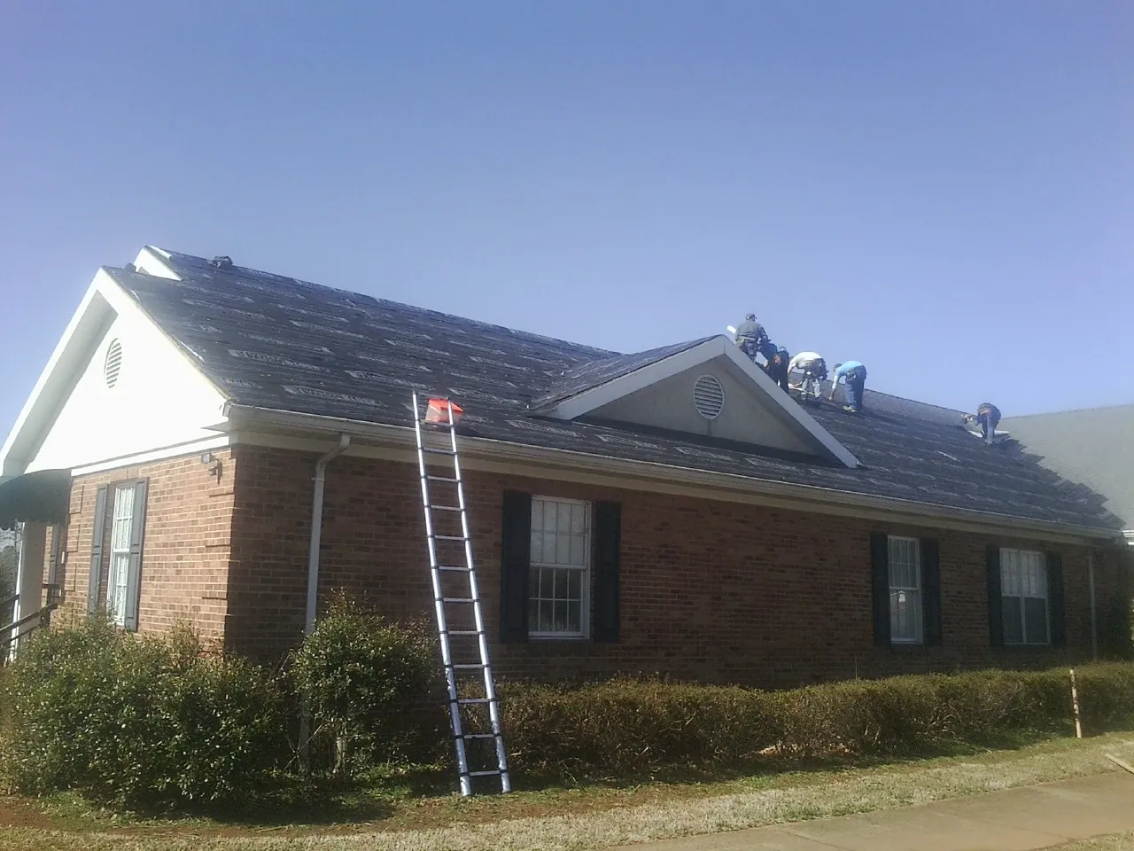Crew tearing shingles off a brick ranch roof with a ladder set — Emergency Roof Repair work by our crew in Beaver Crossing