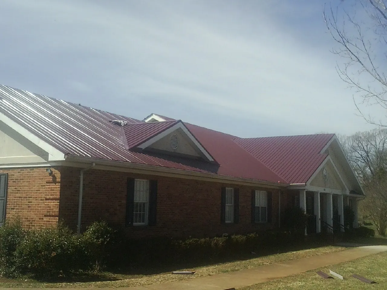 Red metal roof with gabled entries on a long brick building, from a Hail Damage Roof Repair job in Beaver Crossing