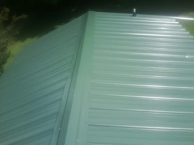 New green metal panels meeting at the ridge of a roof — Flat Roof Repair work by our crew in Beaver Crossing