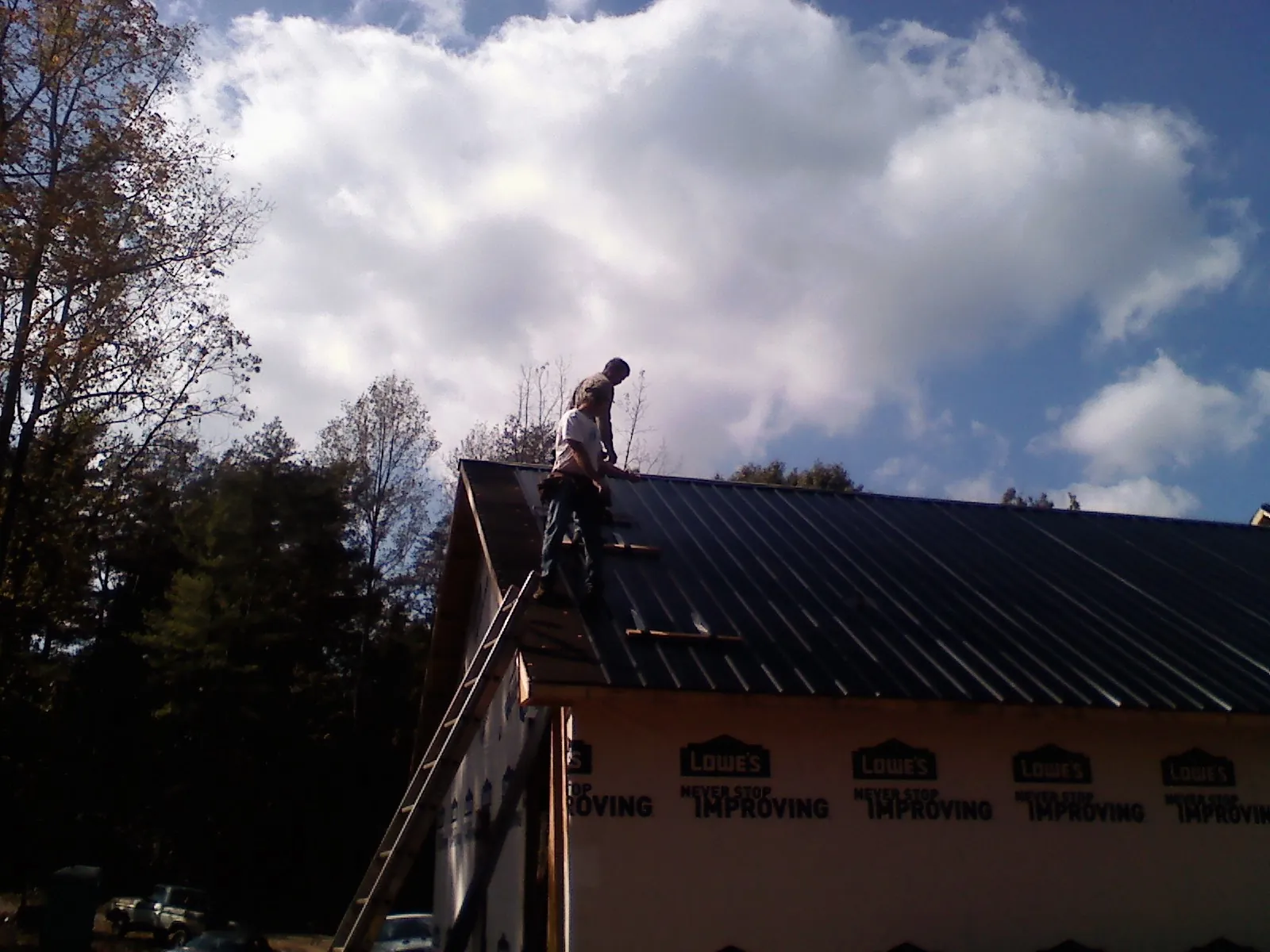 Roofer fastening dark metal panels high against a cloudy sky, from a Roof Inspection job in Beaver Crossing