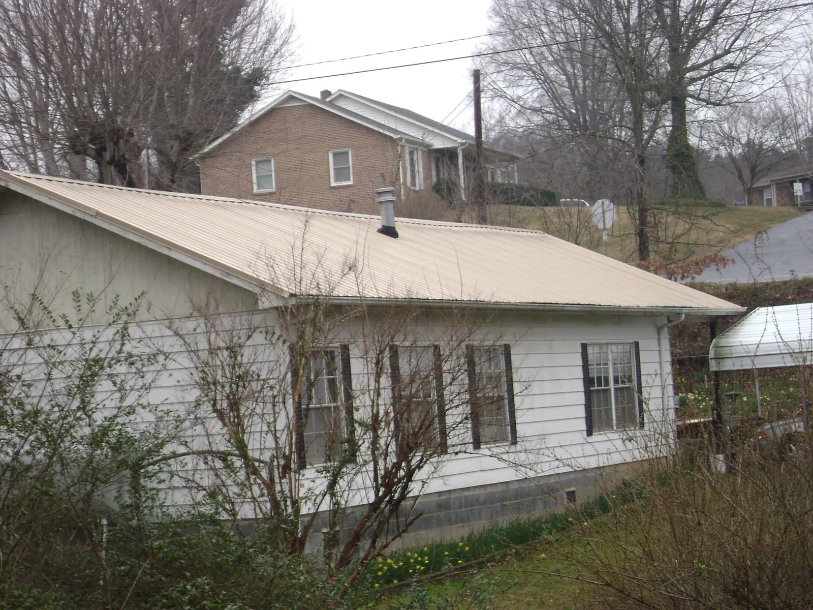 Tan metal roof on a white sided house set into a hillside — Commercial Roofing by Roofing Brothers in Beaver Crossing