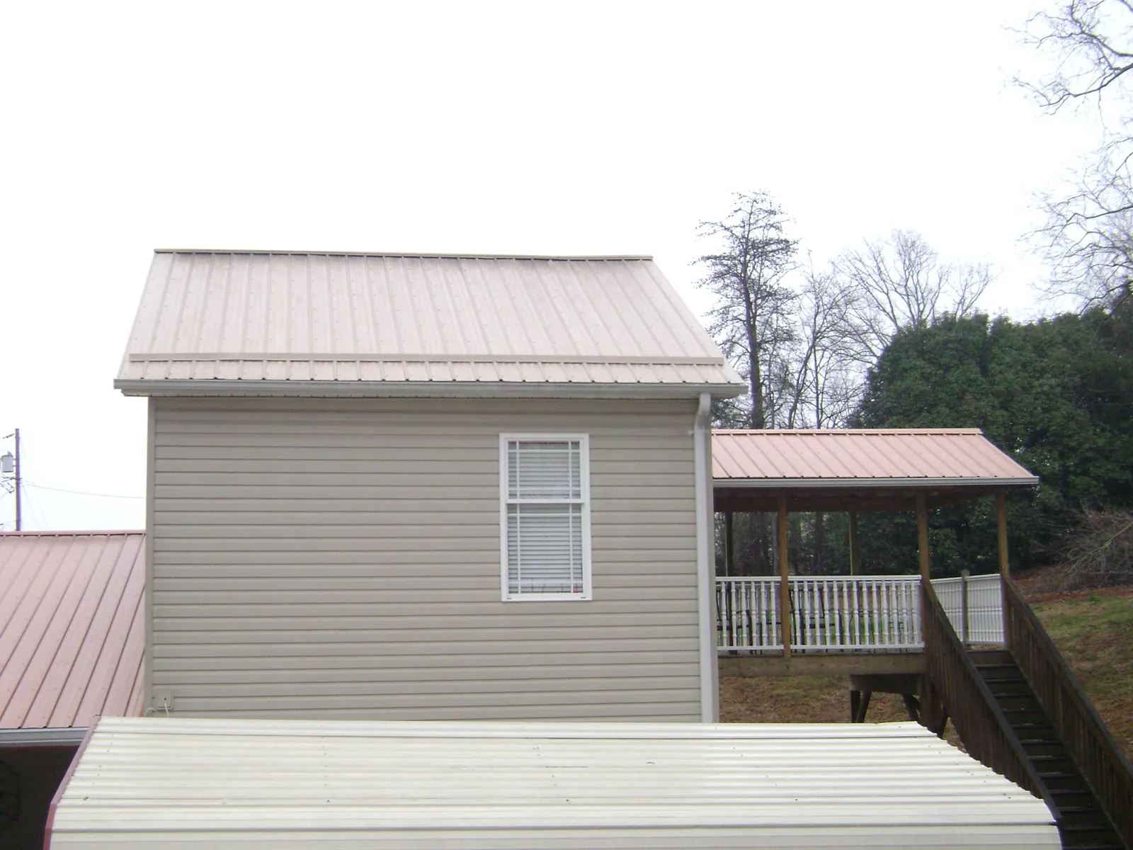 Tan metal roofs on a two story addition and attached porch, from a Roof Replacement job in Beaver Crossing